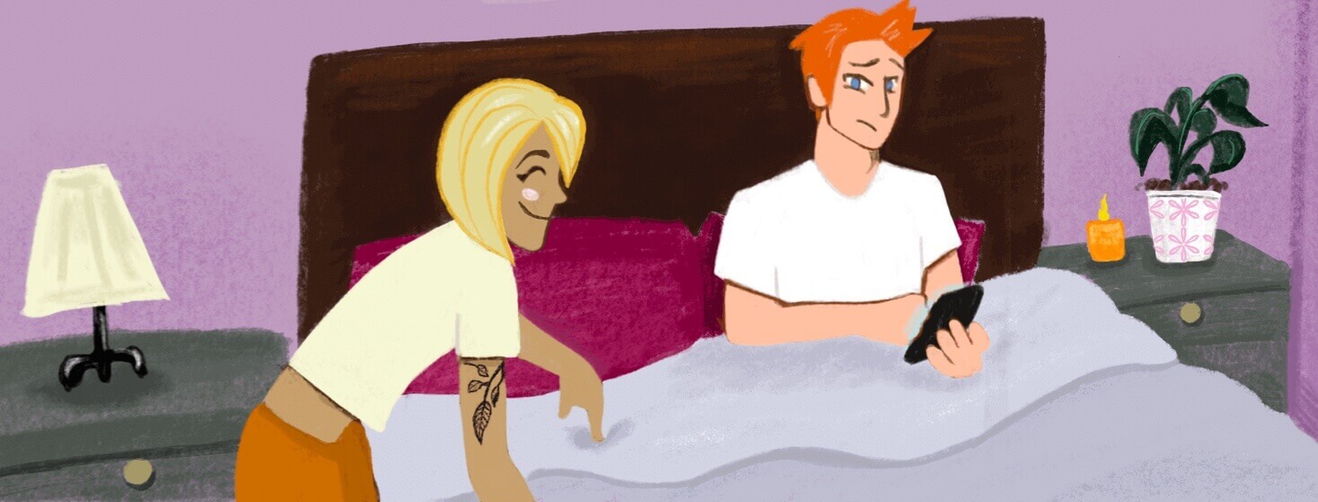 A tan woman with a tattoo points at one side of the bed while a man with red hair is settled in bed on the other side on his phone.